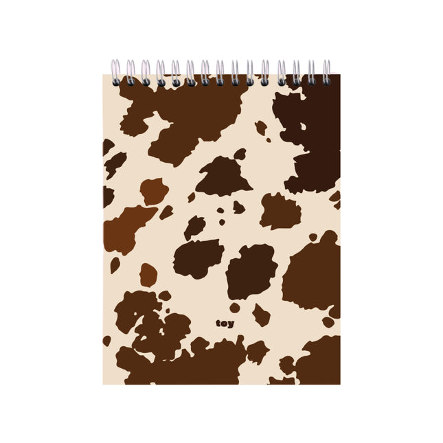 Bitácora Toy Cow Print en tamaños carta y oficio, con 50 hojas blancas sin líneas, portada con estampado de vaca y argollado plástico sobre fondo blanco.