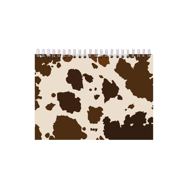 Bitácora Toy Cow Print en tamaños carta y oficio, con 50 hojas blancas sin líneas, portada con estampado de vaca y argollado plástico sobre fondo blanco.