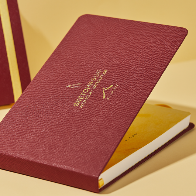 Sketchbook Alpen Acuarela 22×14 cm abierto color vinotinto, tapa dura con banda elástica roja, 24 hojas de 300 g para técnicas húmedas.