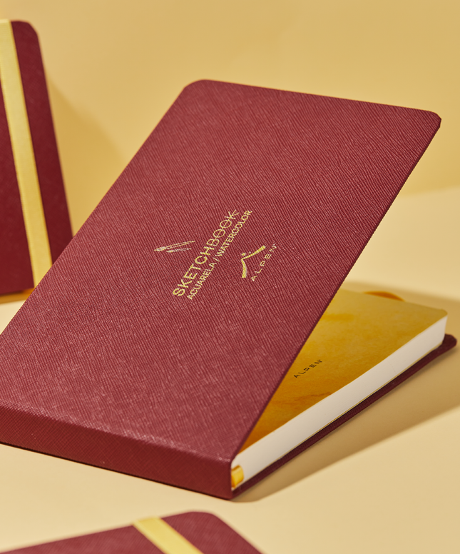 Sketchbook Alpen Acuarela 22×14 cm abierto color vinotinto, tapa dura con banda elástica roja, 24 hojas de 300 g para técnicas húmedas.