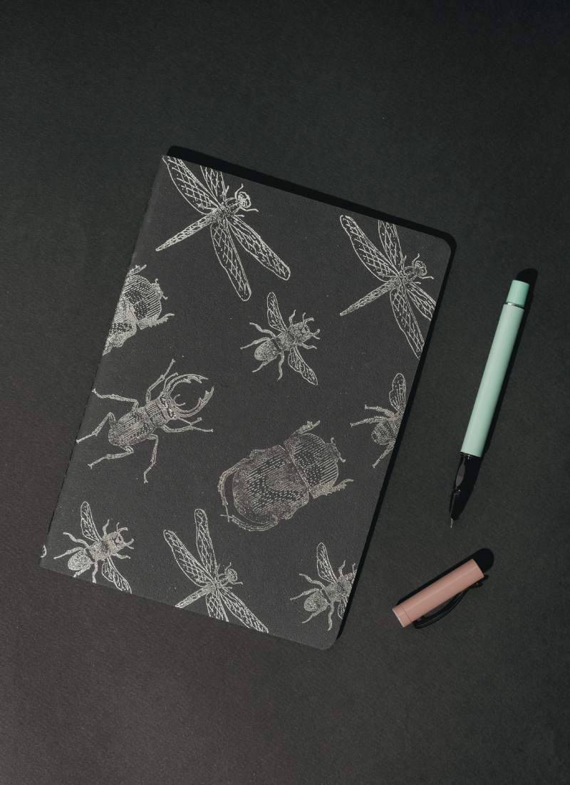 Libreta Econotas Alpen 15×21 cm color negro con ilustraciones de insectos en foil plateado y 32 hojas ecológicas cosidas en hilo.